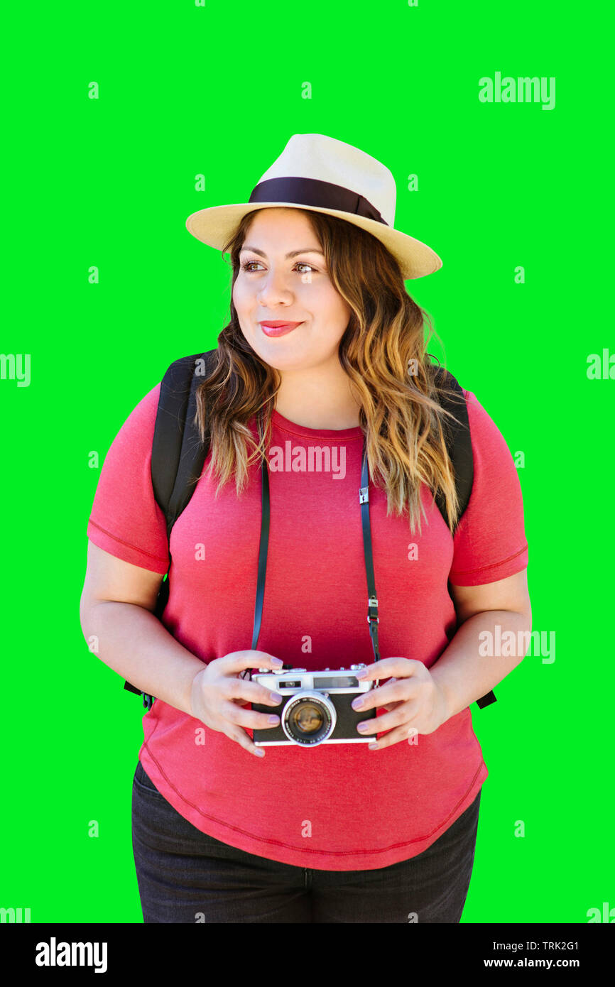 Latina donna millenario detiene una vecchia macchina fotografica mentre si è in viaggio e indossa una fedora Foto Stock