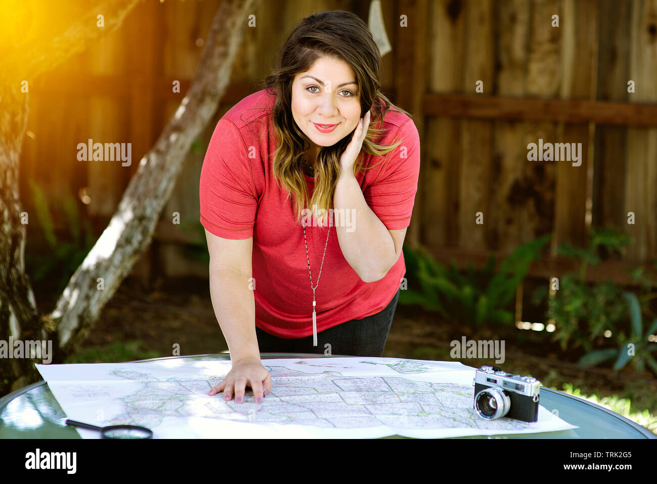 Una giovane donna di latina prevede il suo viaggio con una mappa e una telecamera in illuminazione calda Foto Stock