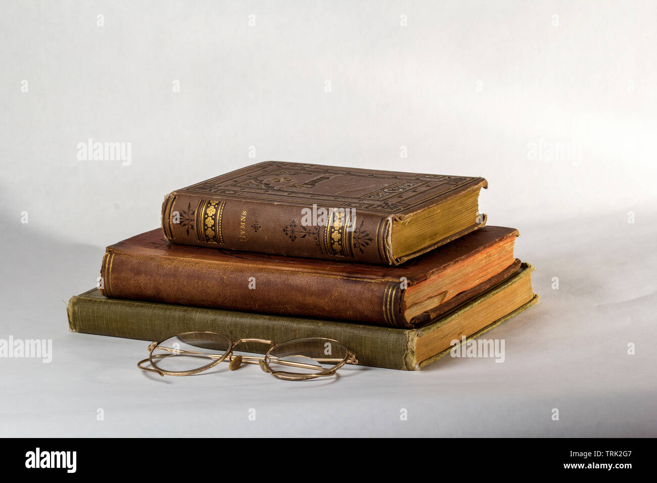 Pila di tre libri antichi con un paio di occhiali vintage su uno sfondo bianco. Foto Stock