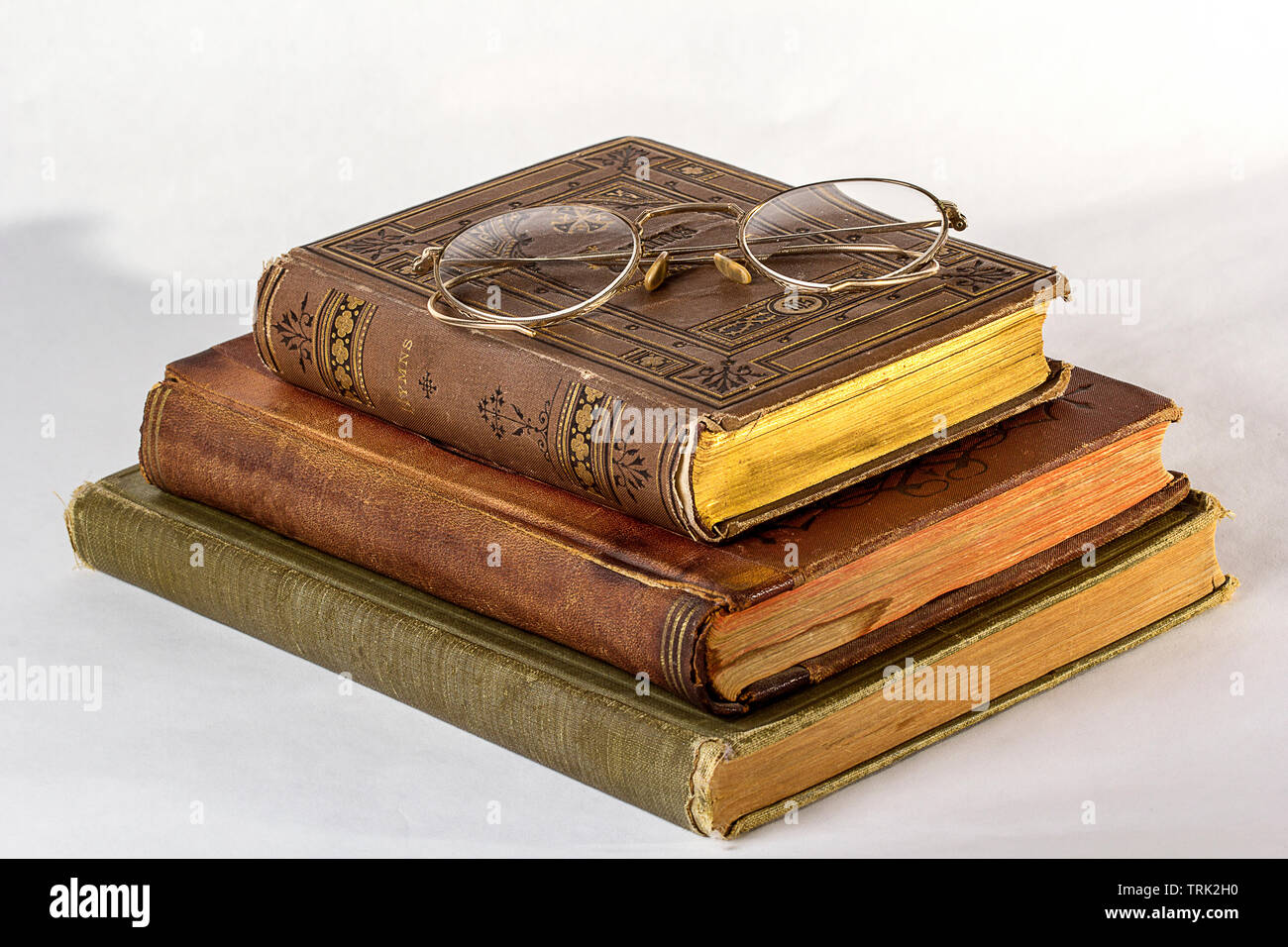 Pila di tre libri antichi con un paio di occhiali vintage su uno sfondo bianco. Foto Stock