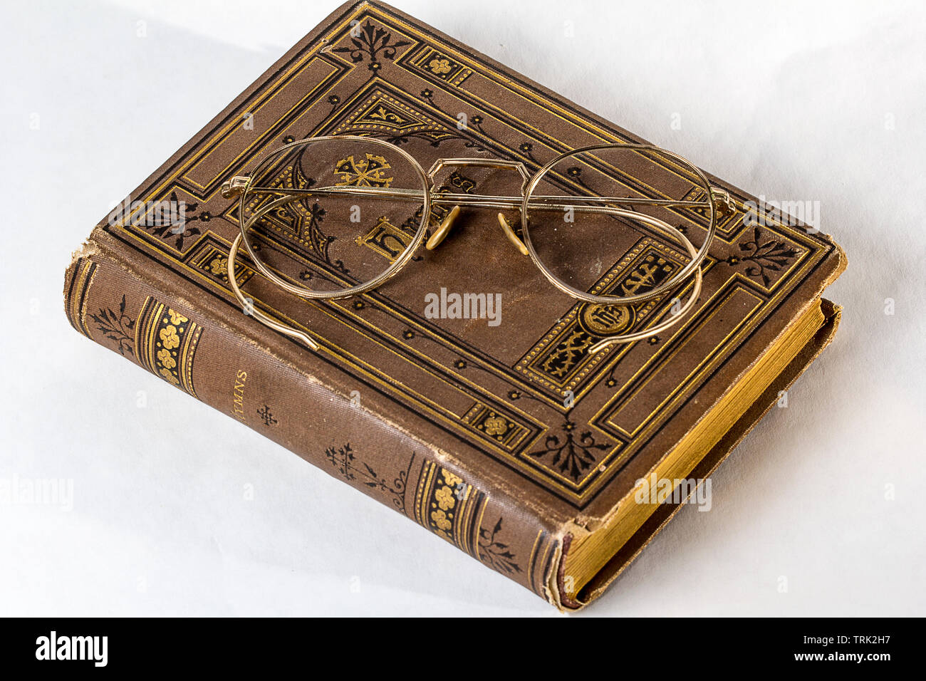 Un paio di occhiali antichi seduti su un vintage hymnal su uno sfondo bianco. Foto Stock