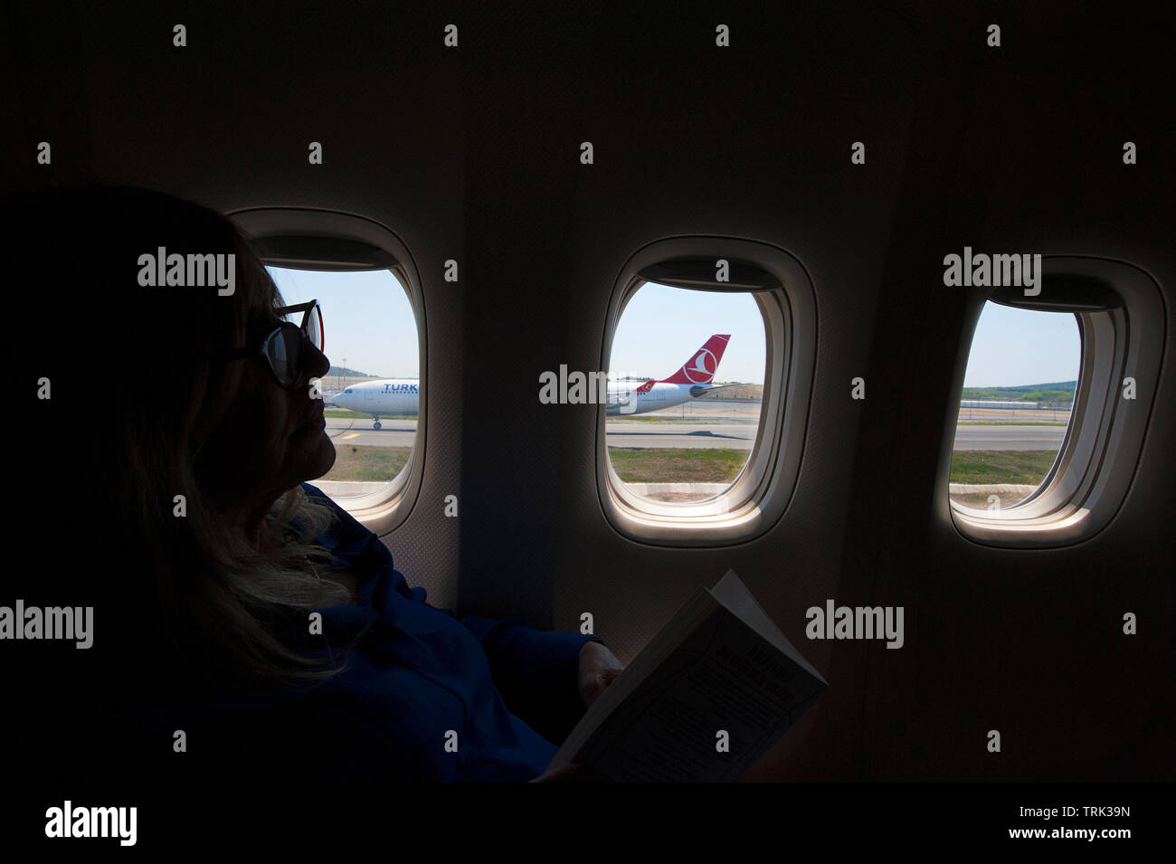 Una donna si rilassa in nella sezione business class di Turksih Airlines come taxi sulla pista con la vista di un volo in arrivo. Foto Stock