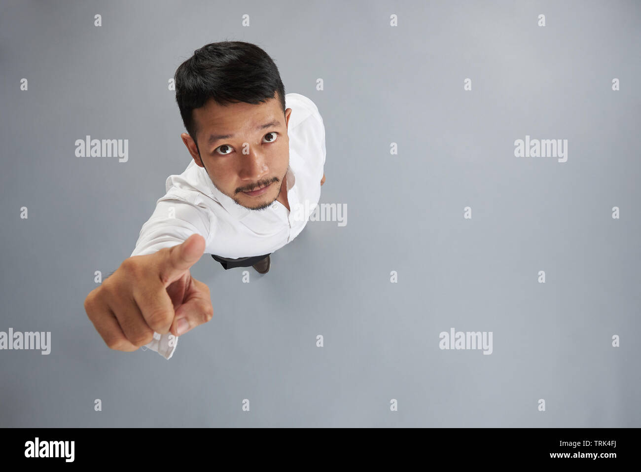 Asian giovane uomo punto dito per fotocamera sopra vista dall'alto isolato su sfondo grigio Foto Stock