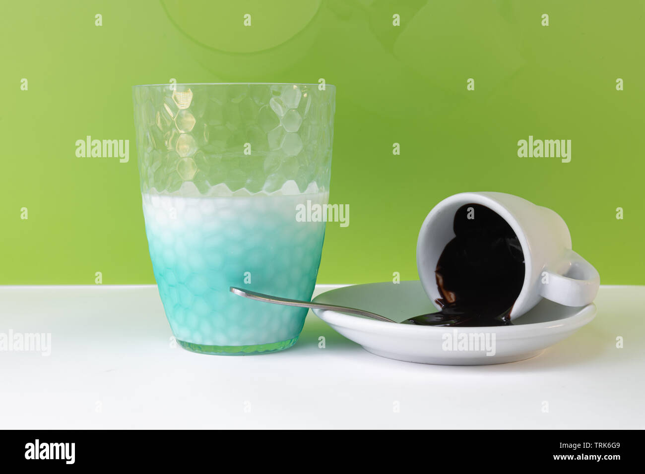 Cioccolato fondente versato dalla tazza di caffè e un mezzo bicchiere di latte, isolato su sfondo verde vicino fino Foto Stock