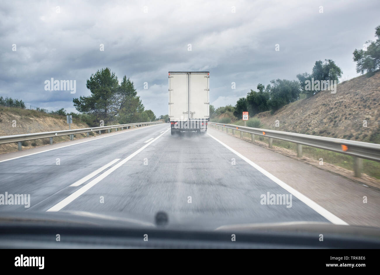 Guida dietro lento carrello su strada locale in un giorno di pioggia. Vista dall'interno della vettura Foto Stock