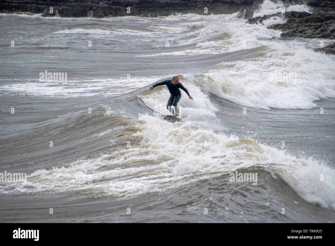 Una mezza età surfer in mute hols il suo equilibrio in acqua difficile. Resto Bay Porthcawl, Regno Unito. Foto Stock