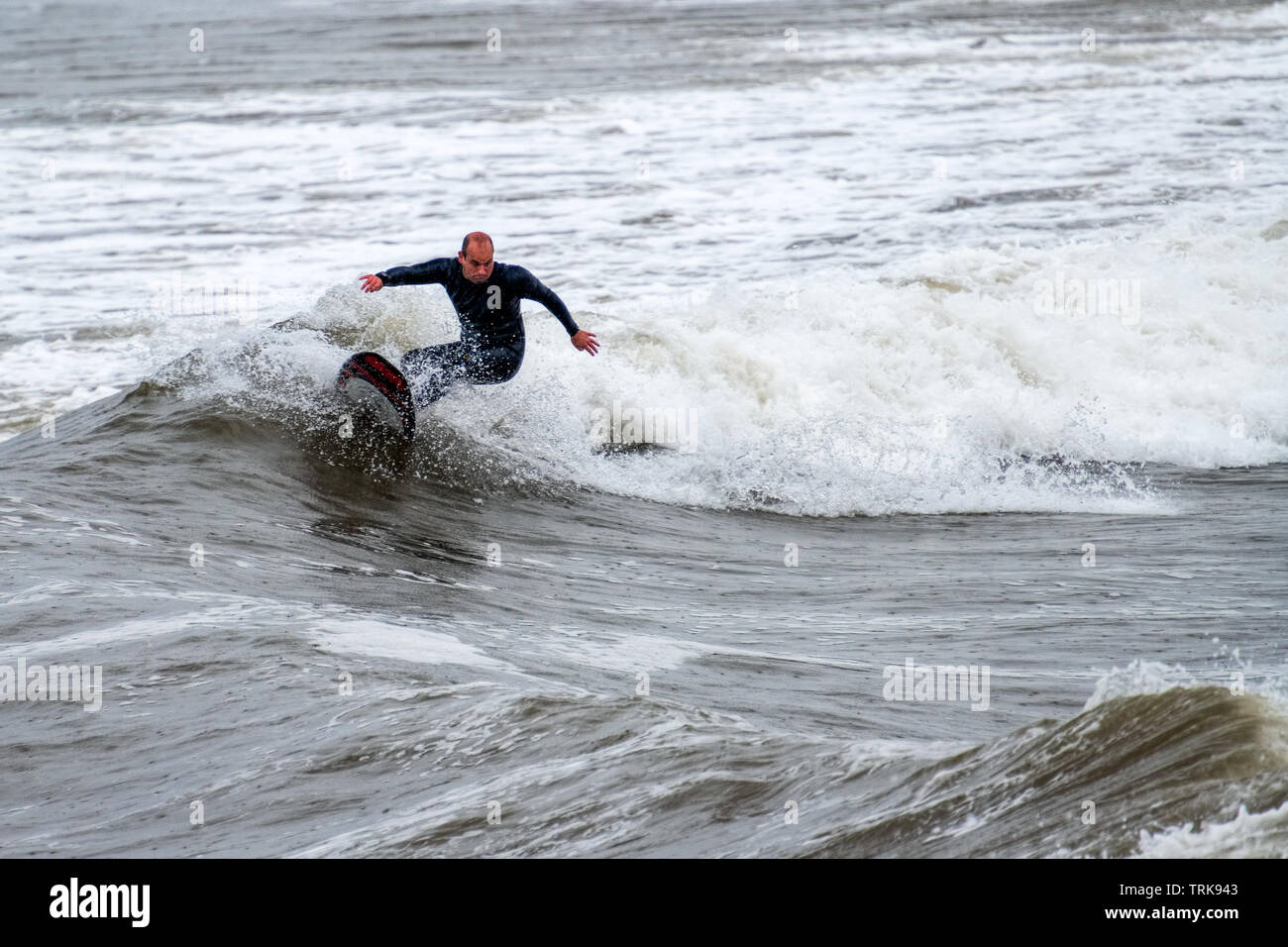 Una mezza età surfer cavalcare le onde sotto la pioggia. Resto Bay, Porthcawl, Regno Unito. Foto Stock
