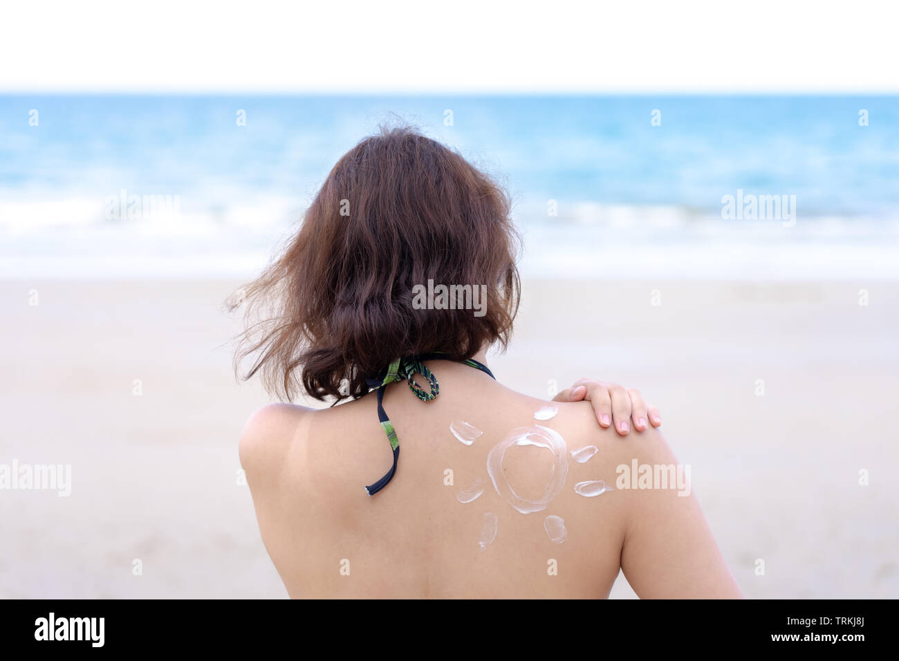 Dehor Estivo ritratto di giovani asiatici tan donna che indossa un bikini seduto sulla spiaggia l'applicazione di crema solare con sun tracciata sulla spalla, vacanze estive. Foto Stock