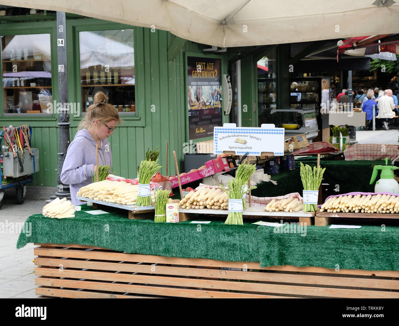 Maggio 2019 - UNA giovane bionda caucasica vende asparagi bianchi da uno stand nel mercato dei vigili di Monaco, Germania Foto Stock