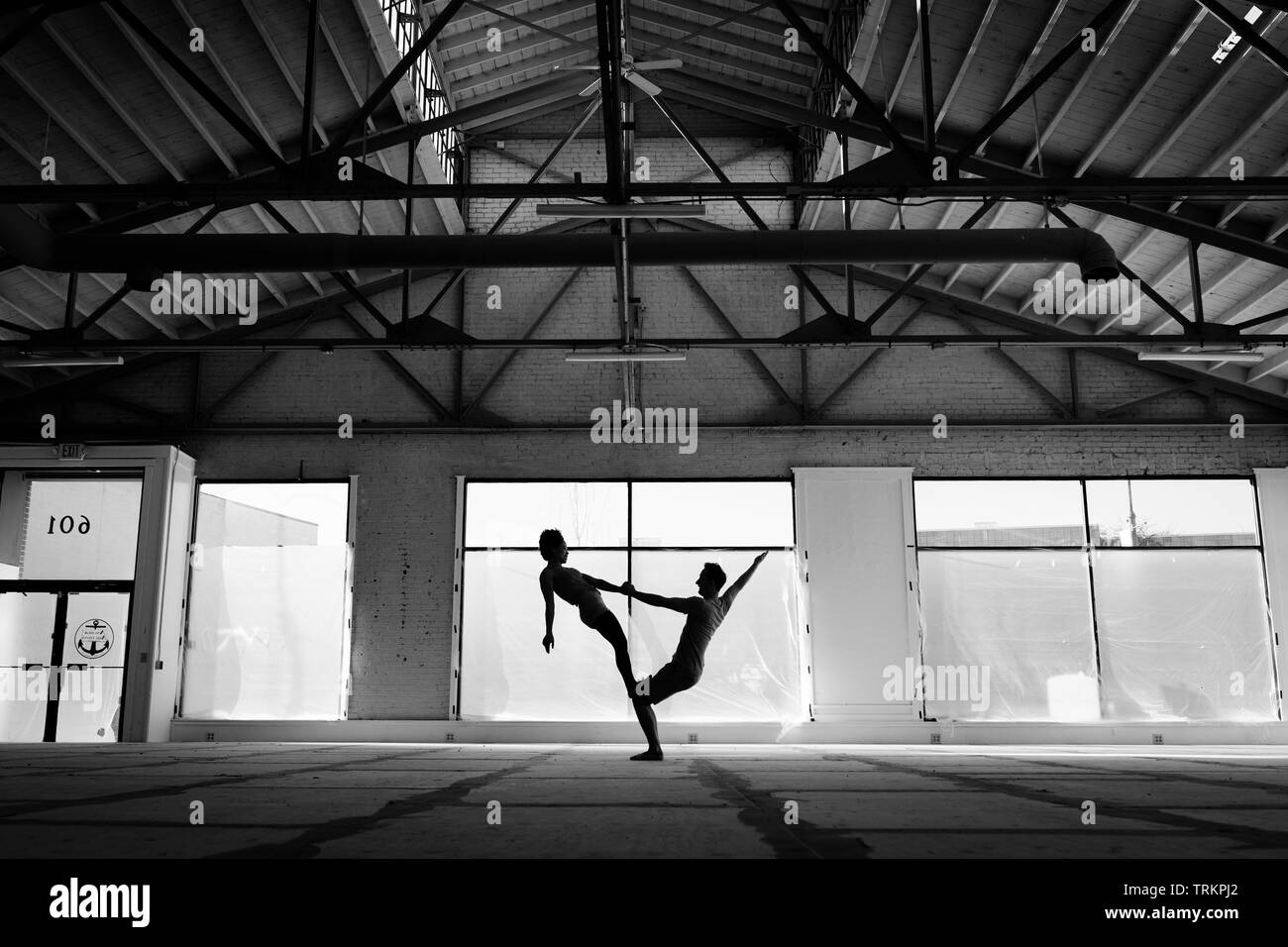 Acro Yoga giovane dimostrando yoga acrobatico si muove in un magazzino di moody in bianco e nero. Foto Stock