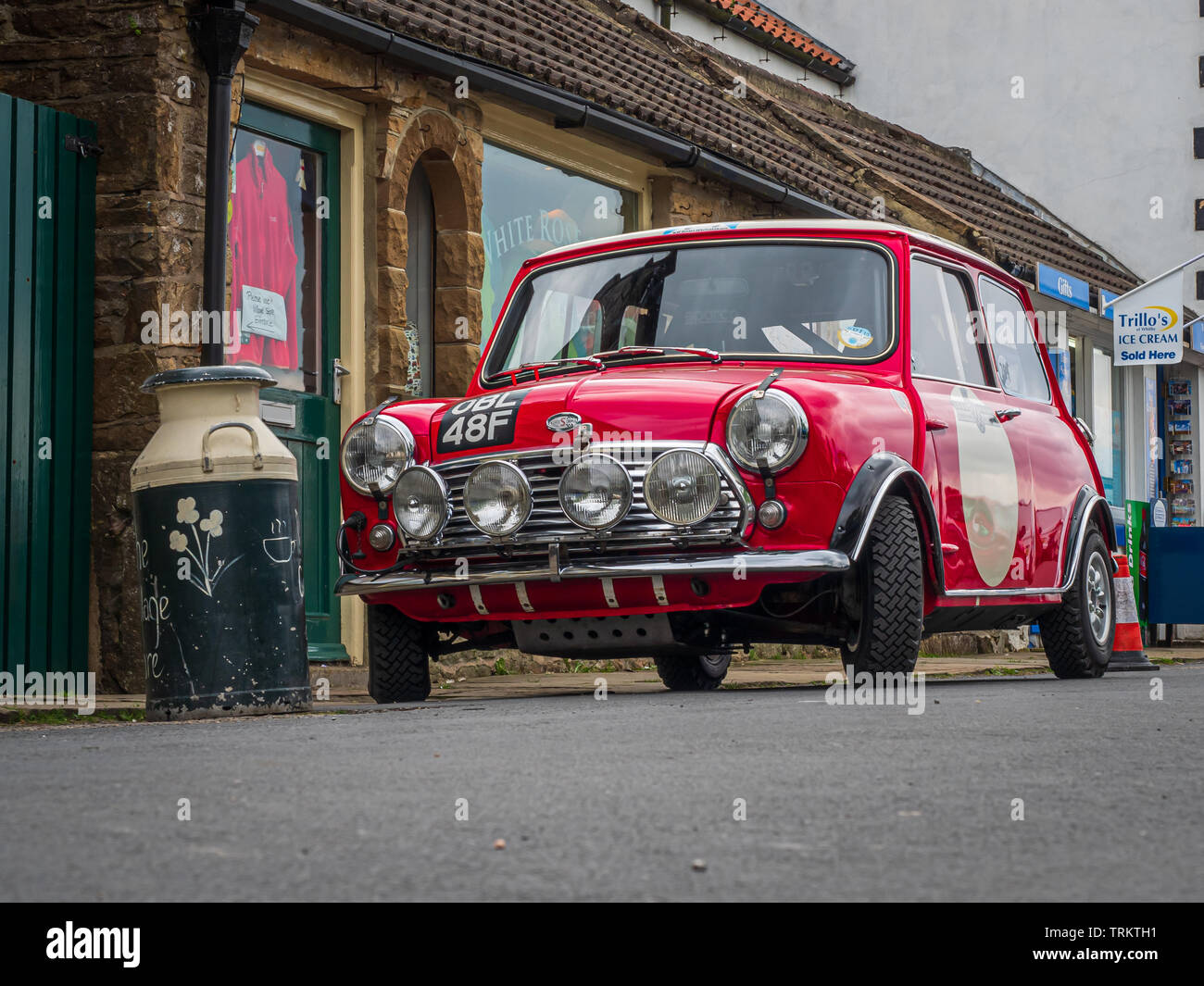 Classic Red Mini Cooper parcheggiato da Vintage Milk Churn in Goathland North Yorkshire l'ambientazione della popolare serie televisiva Heartbeat ambientato negli anni '60 Foto Stock