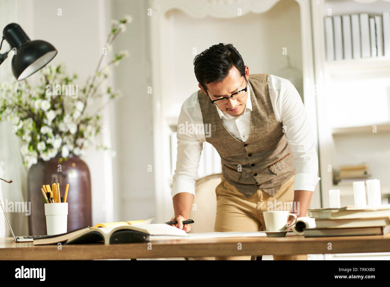 Giovani asiatici architetto designer in piedi fromt del banco di lavoro a casa Foto Stock