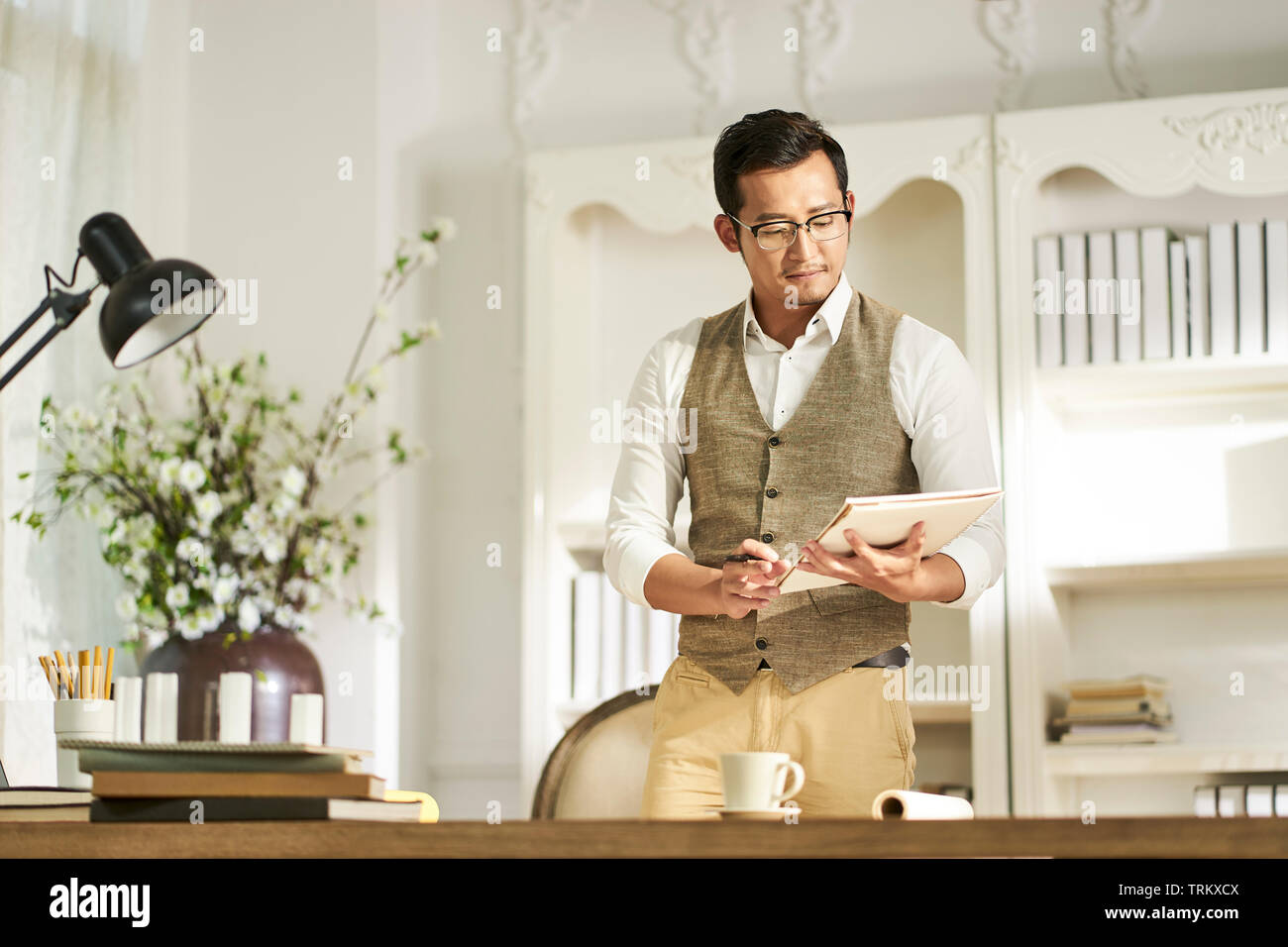 Giovani asiatici architetto designer in piedi fromt del banco di lavoro a casa Foto Stock