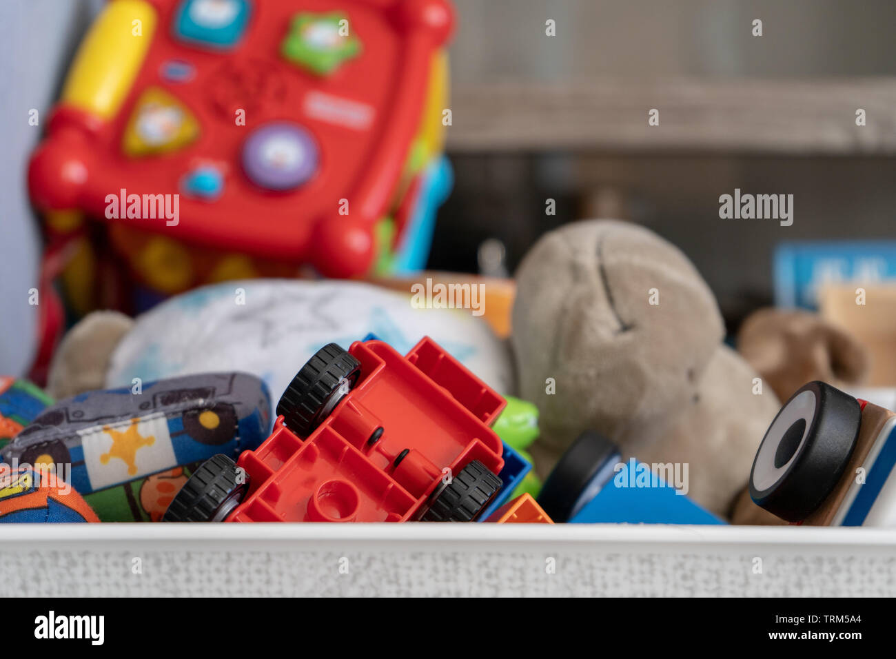 In prossimità di una scatola di giocattoli, con molti oggetti diversi tra cui giocattoli morbidi, riproduzione di automobili e giocattoli per bimbi più grandi. Foto Stock