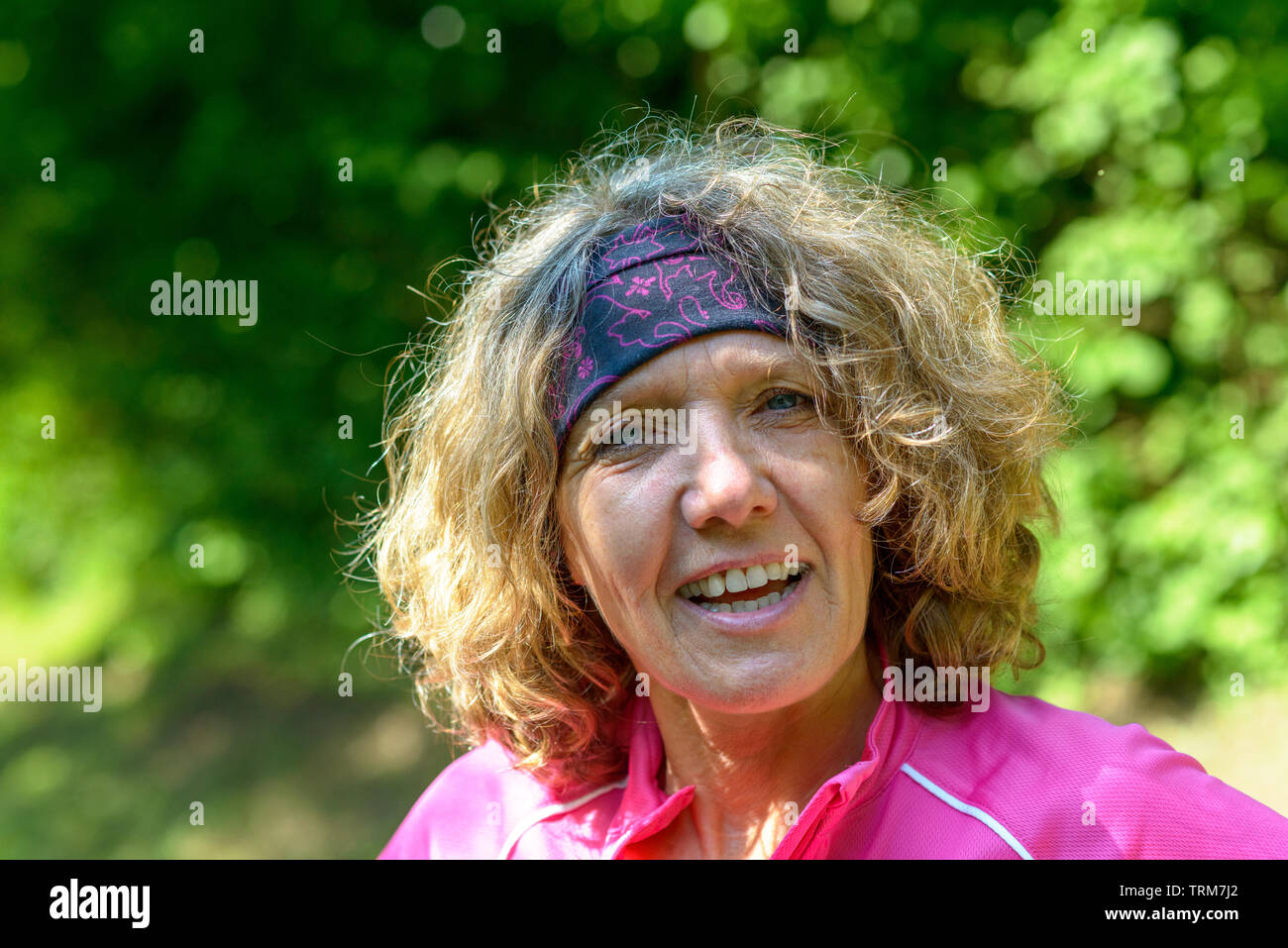 Attraente alla moda donna di mezza età che indossa una banda di testa i quali discutevano animatamente per la telecamera contro uno sfondo di foglia verde fogliame Foto Stock
