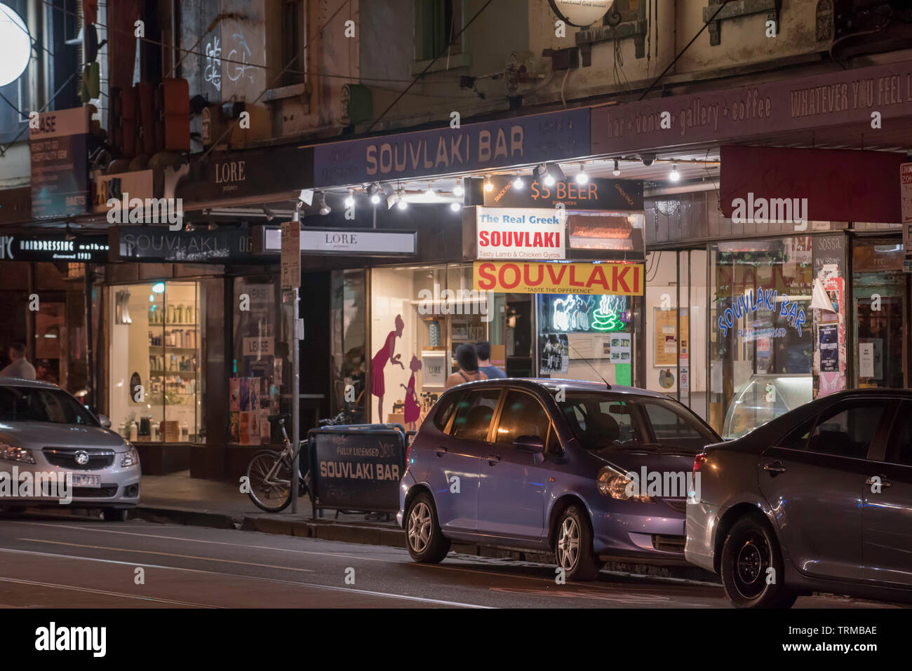 Tempo di notte al di fuori di una fila di negozi tra cui un greco souvlaki bar su Brunswick Street, Fitzroy, Victoria, Australia Foto Stock