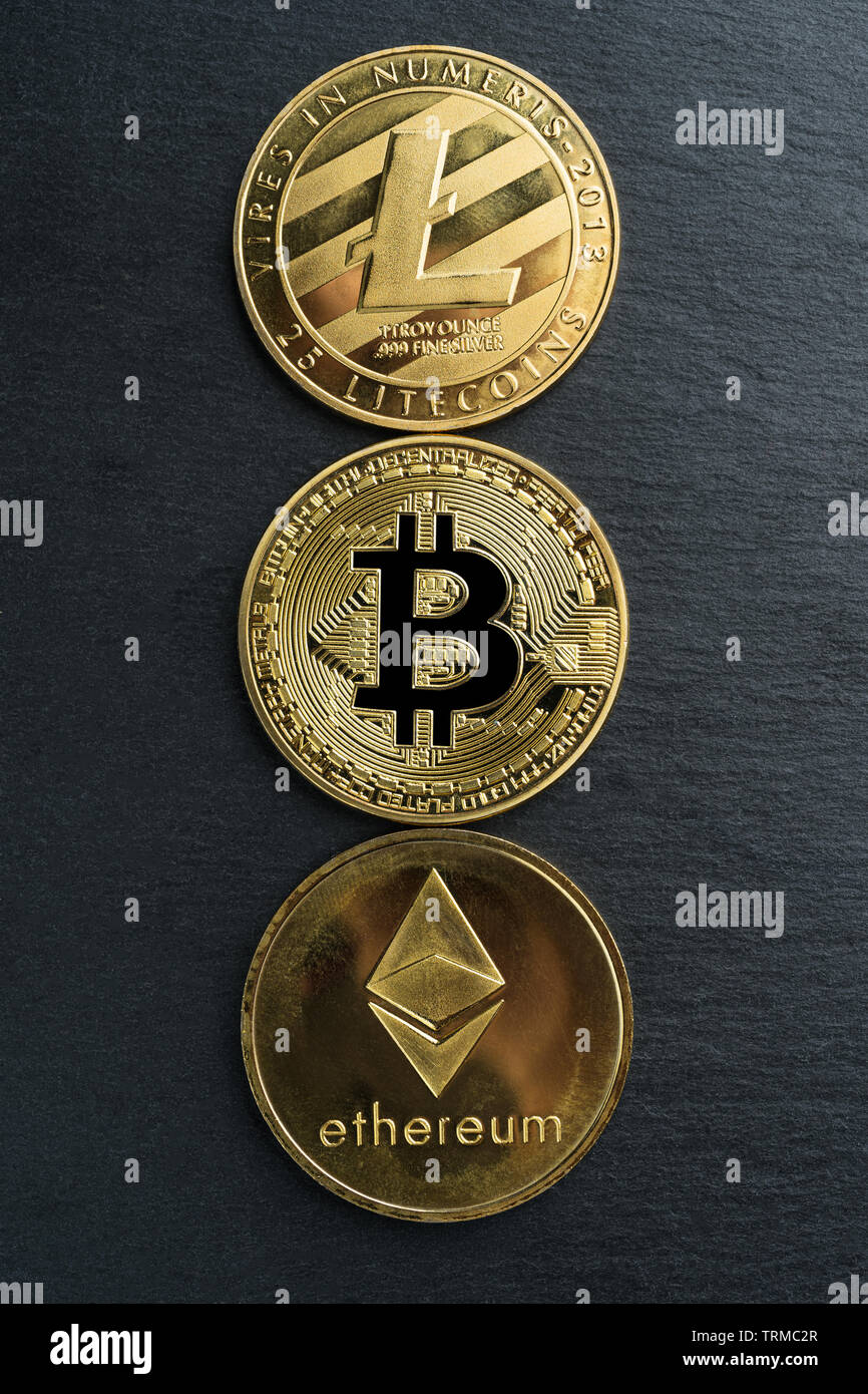 Bitcoin fisico, Litecoin e Ethereum monete d oro su una pietra nera piastra di ardesia sfondo. Cryptocurrency. Orientamento verticale. Foto Stock