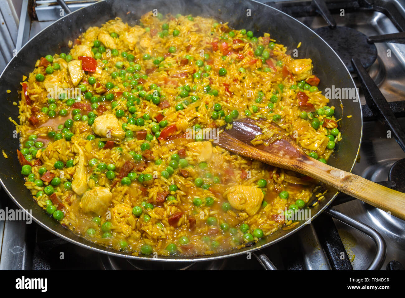 Agitazione paella di pollo con una spatola di legno durante la cottura e piselli verdi e il chorizo Foto Stock