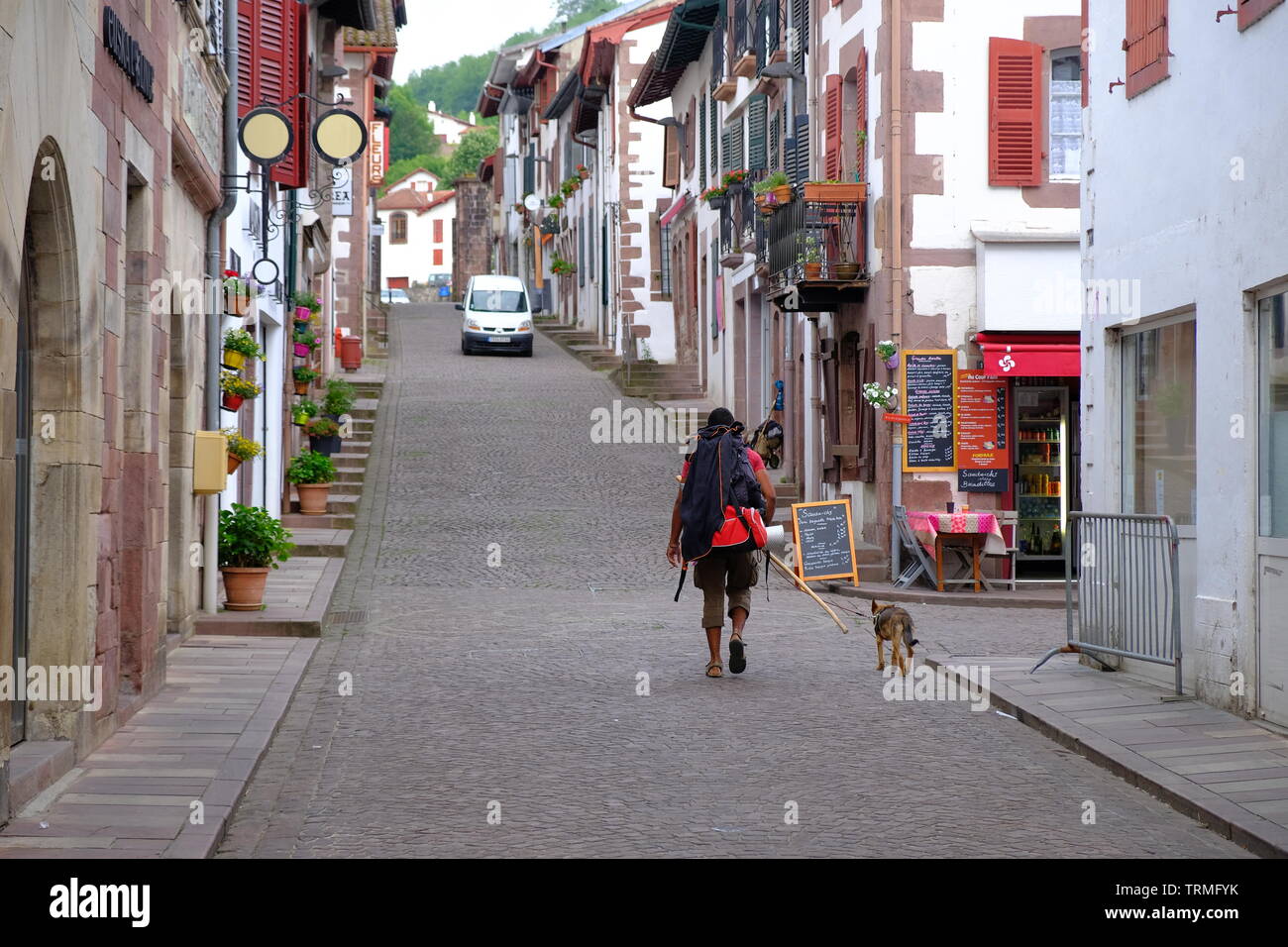 Pellegrino con un cane lasciando la mattina presto sul loro cammino di Santiago sulla via della St-James, strade di St-jean-pied-de-port, Francia, giugno 2019 Foto Stock