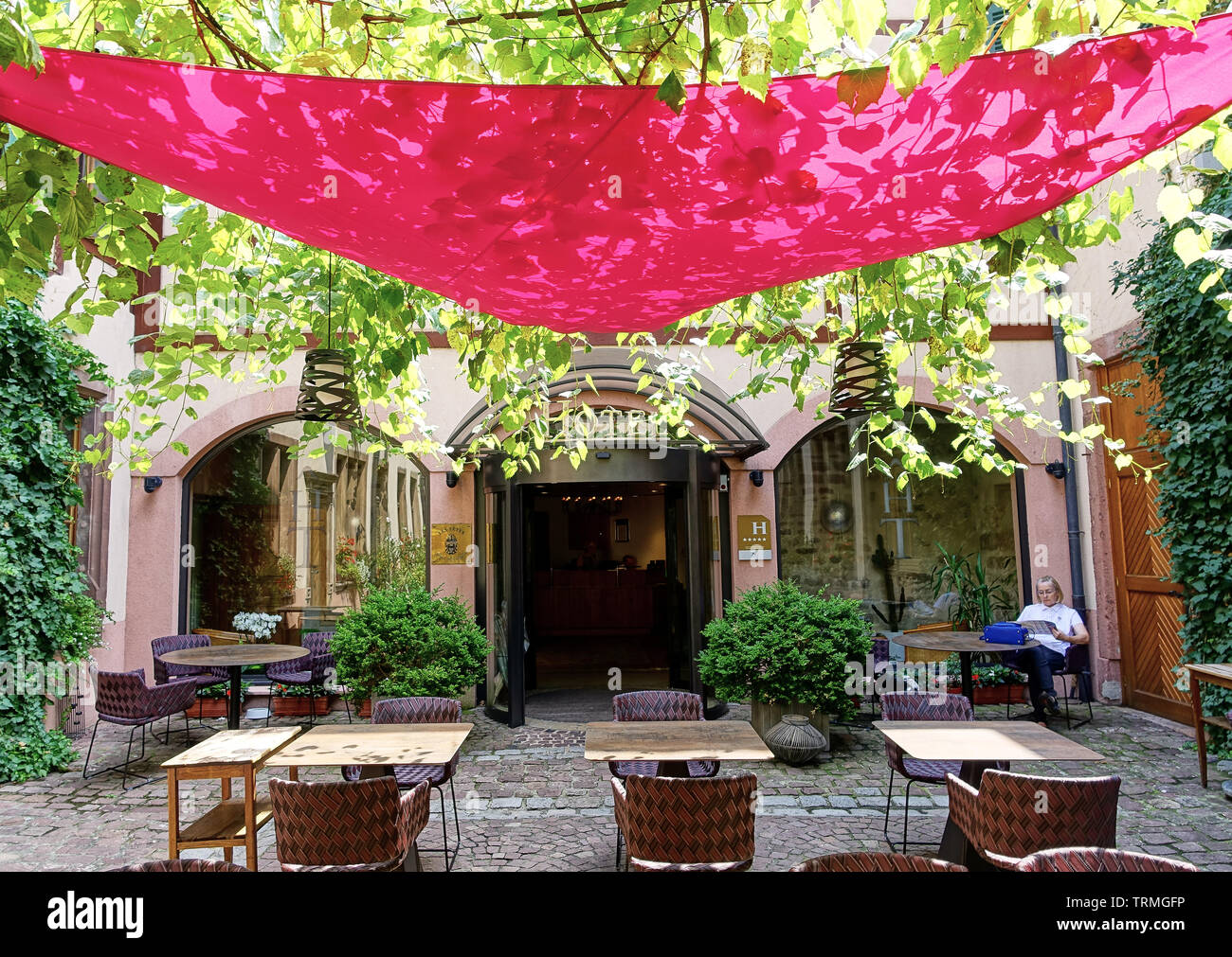 Colmar, Francia - Agosto 2015: Hotel Courtyard con bellissimo baldacchino rosso e verde di un incantevole all'aperto ombreggiata area pranzo. Donna quotidiano di lettura. Foto Stock