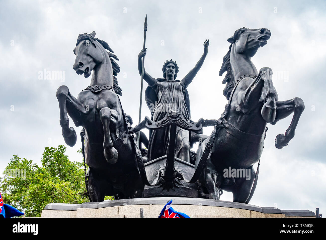 Un basso angolo di visione di una statua di bronzo di Boudica a cavallo di un carro trainato da due cavalli visto da un angolo basso contro il grigio di un cielo nuvoloso. Foto Stock