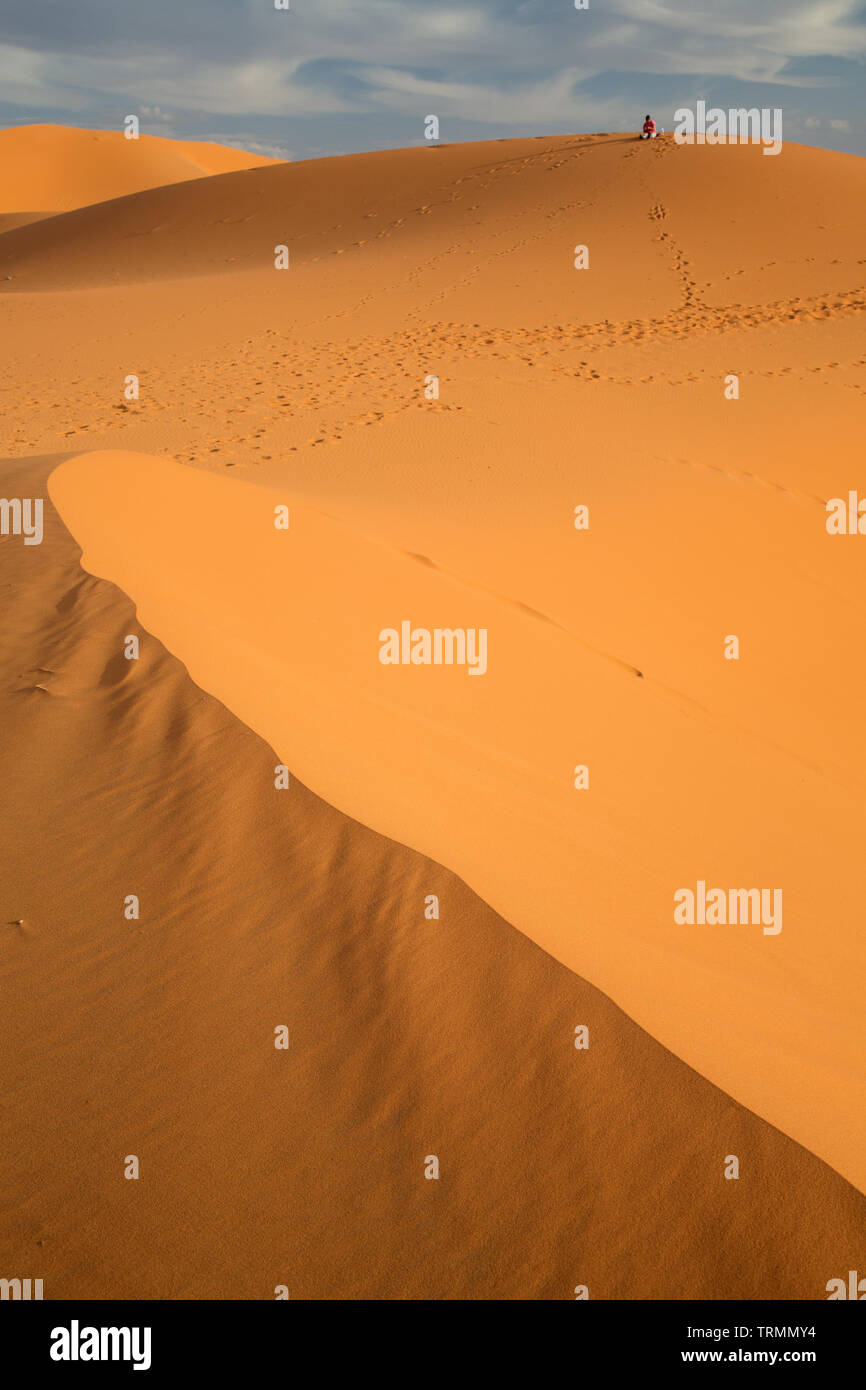 Un lone persona siede sulla cima di una duna di sabbia nel deserto del Sahara in Marocco Foto Stock