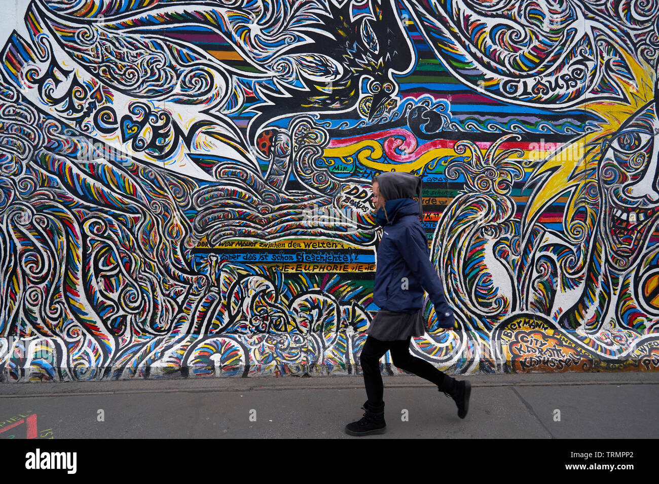 Una donna cammina davanti Schamil Gimajev di lavoro su una parte del muro di Berlino. Foto Stock