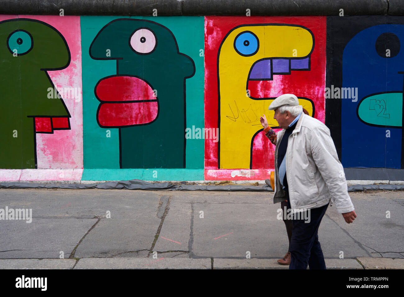 Un giovane cammina davanti a Thierry Noir di lavoro su una parte del muro di Berlino. Foto Stock