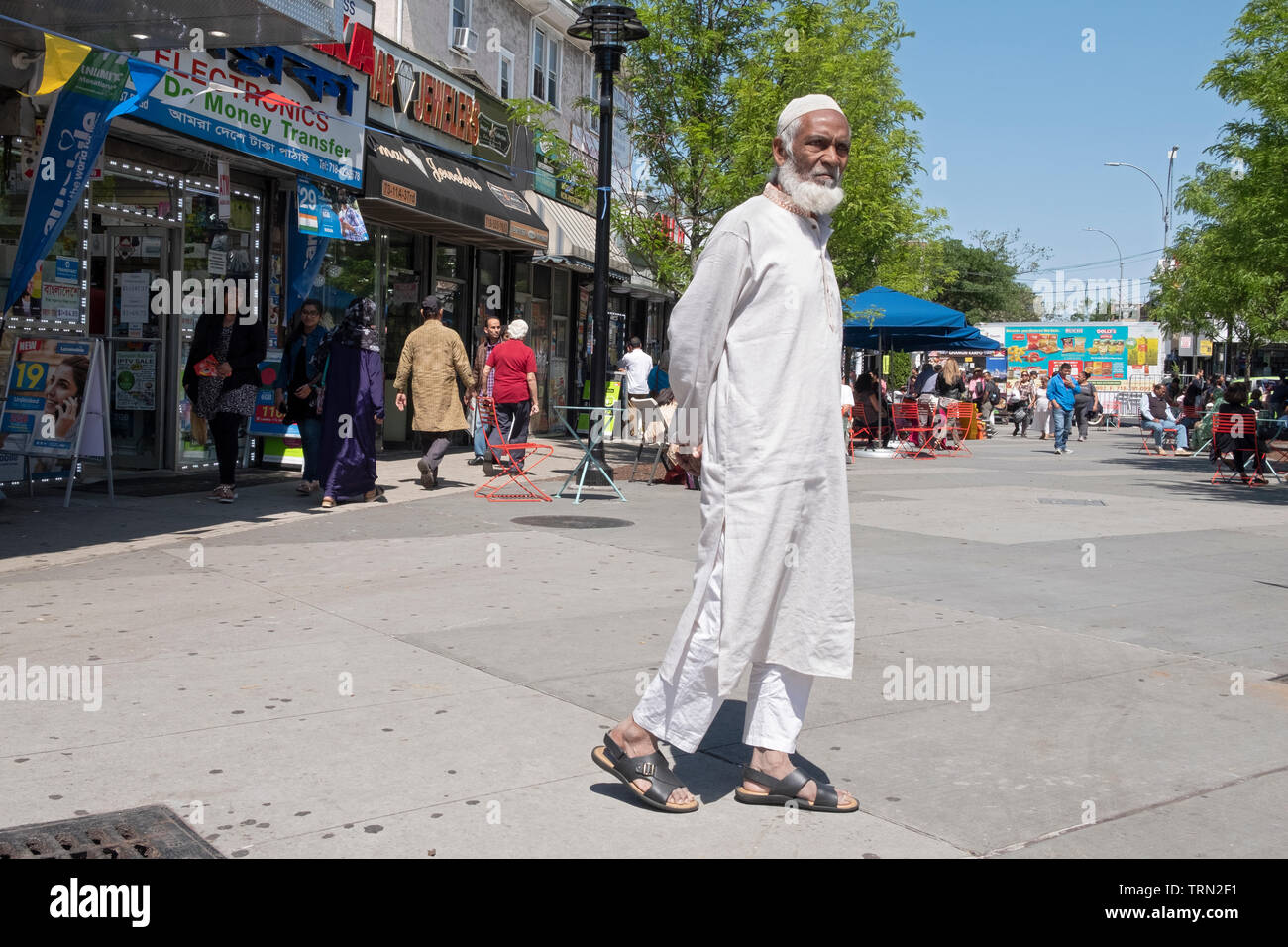 Un uomo musulmano in tradizionali abiti etnici camminando nella diversità Plaza in Jackson Heights, Queens, a New York Foto Stock