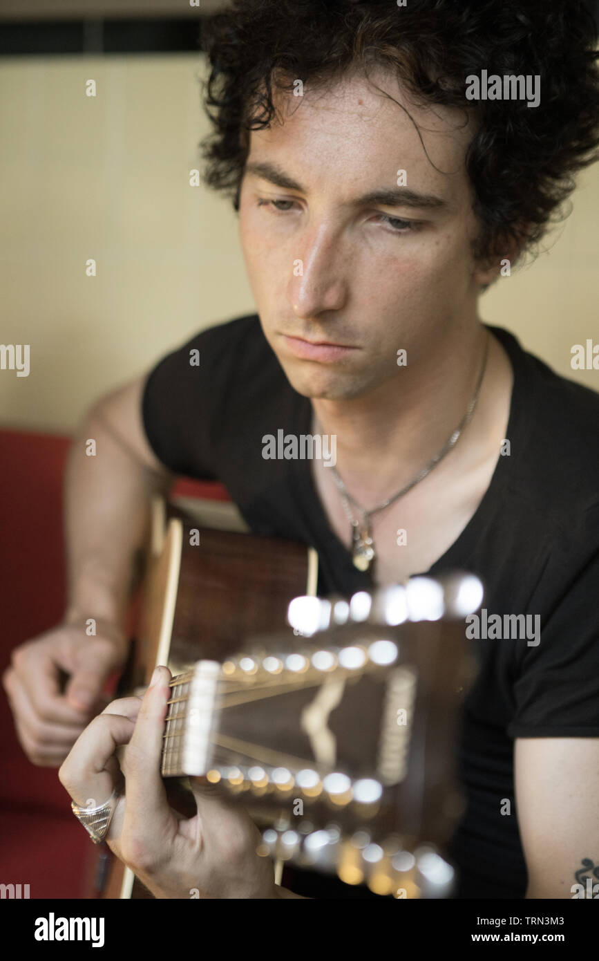 Giovane uomo suona la chitarra su un divano Foto Stock