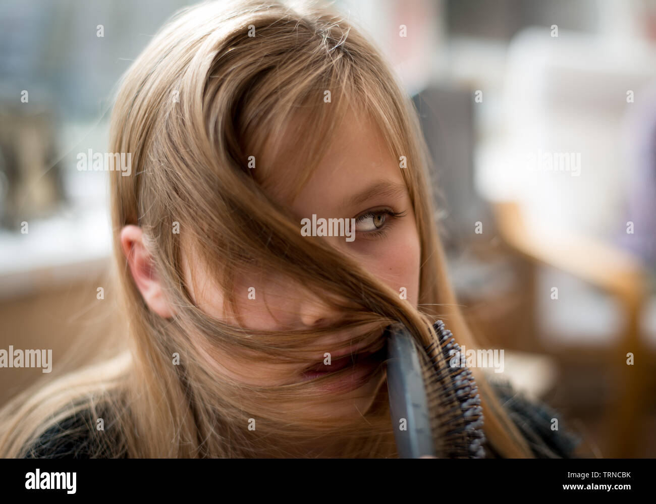 Bella ragazza bionda sta spazzolando i capelli e guardando coy Foto Stock
