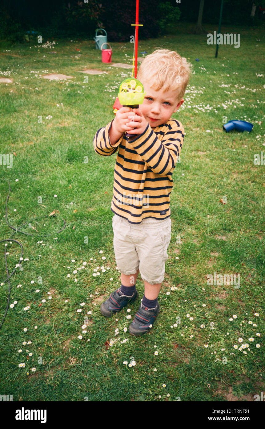 Due anni di vecchio ragazzo giocando fuori con un giocattolo Pistola bolle, Medstead, Alton, Hampshire, Inghilterra, Regno Unito. Foto Stock