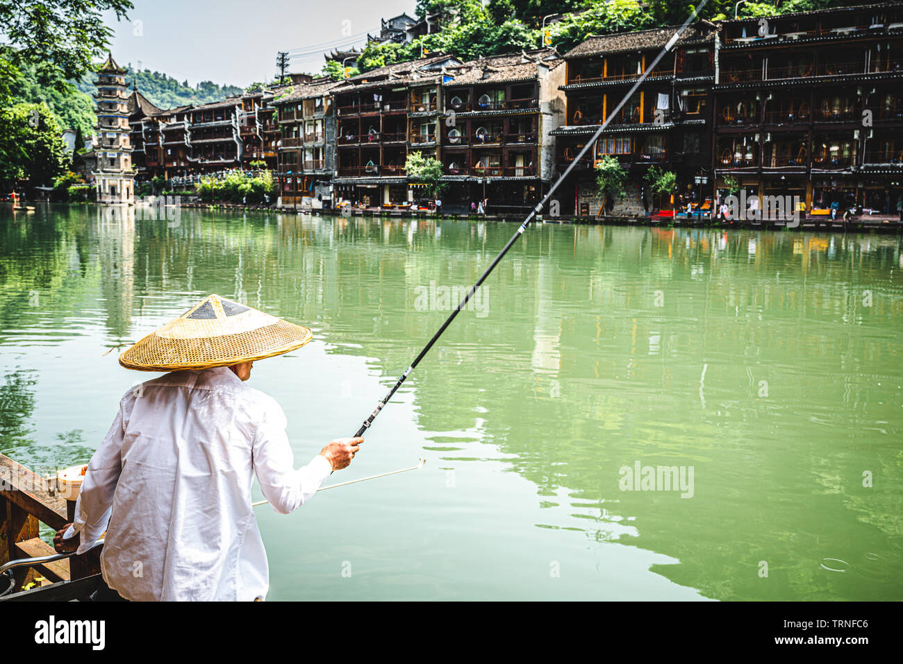 Pescatore cinese indossando un asiatico cappello conico e scenario di Fenghuang antica città di Phoenix in background in Cina Hunan Foto Stock