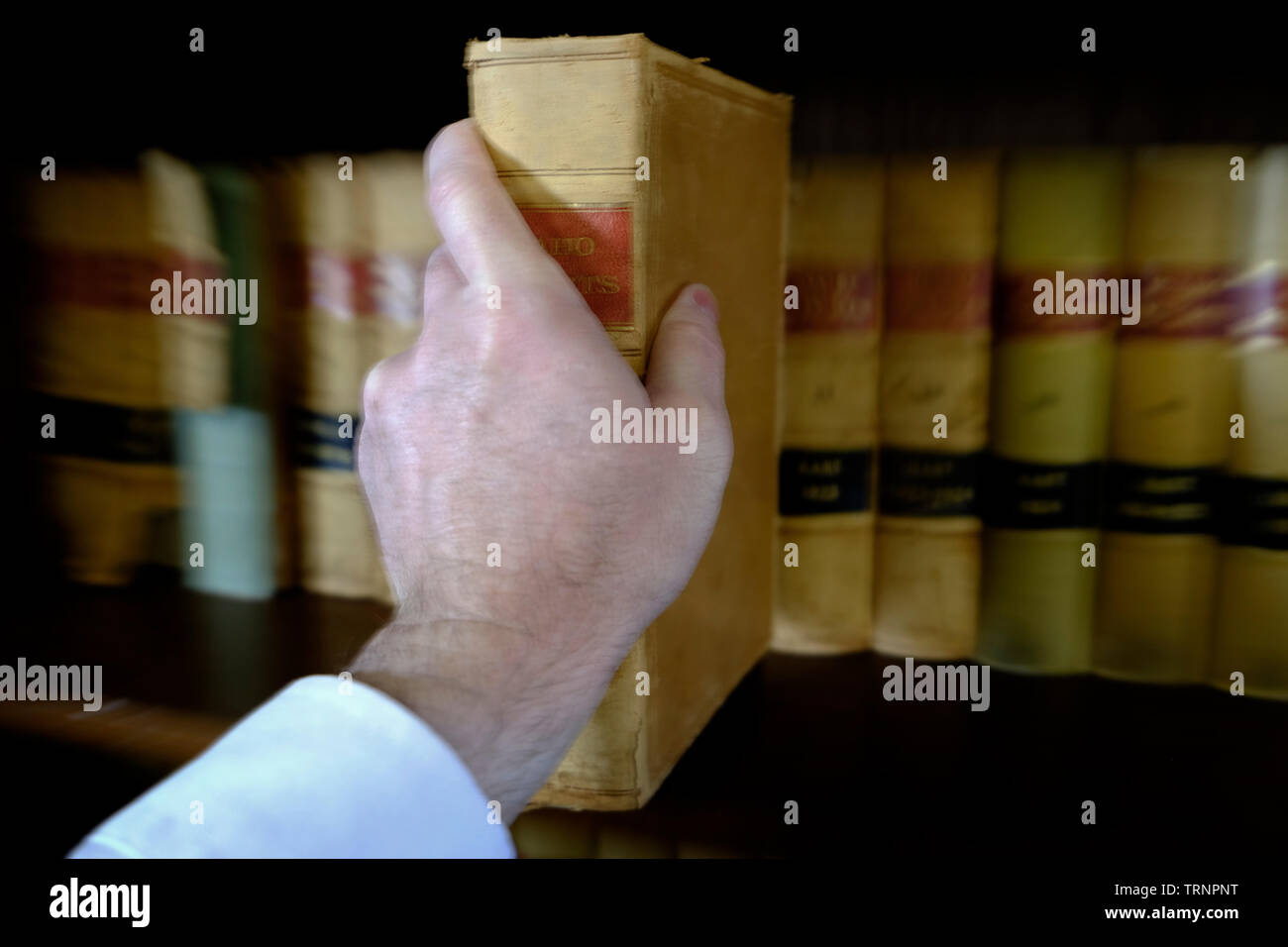 La mano di raggiungere per prenotare tirando fuori scaffale in biblioteca Foto Stock