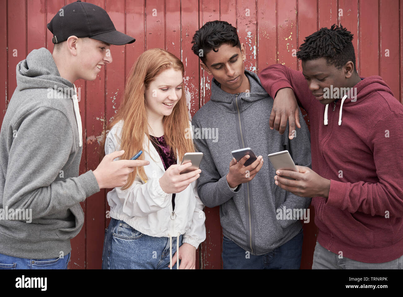 Gruppo di amici adolescenti guardando i telefoni cellulari nel contesto urbano Foto Stock