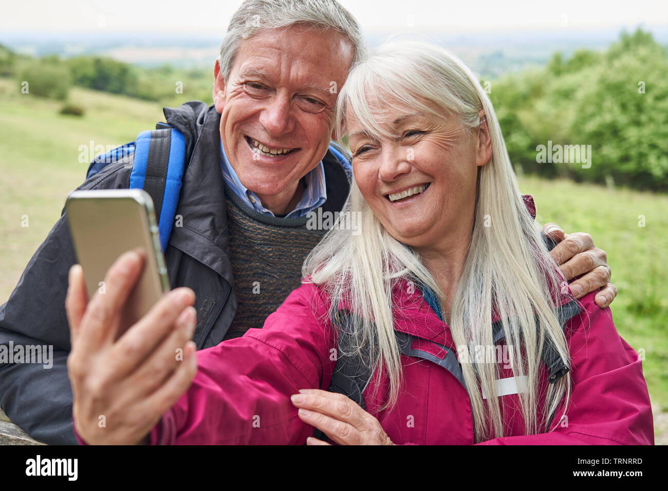 Sorridente coppia Senior escursionismo in campagna in piedi da Gate e tenendo Selfie sul telefono cellulare Foto Stock