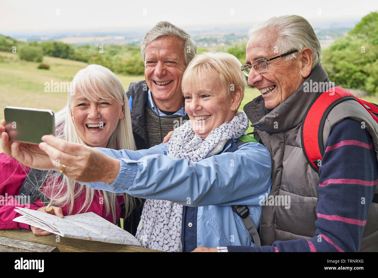 Gruppo di amici Senior escursionismo in campagna in piedi da Gate e tenendo Selfie sul telefono cellulare Foto Stock