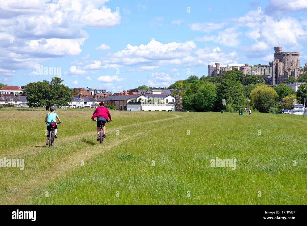 Una giovane coppia in bicicletta sulle Brocas dal fiume Tamigi su una giornata d'estate con il Castello di Windsor in background, Eton Berkshire England Regno Unito Foto Stock