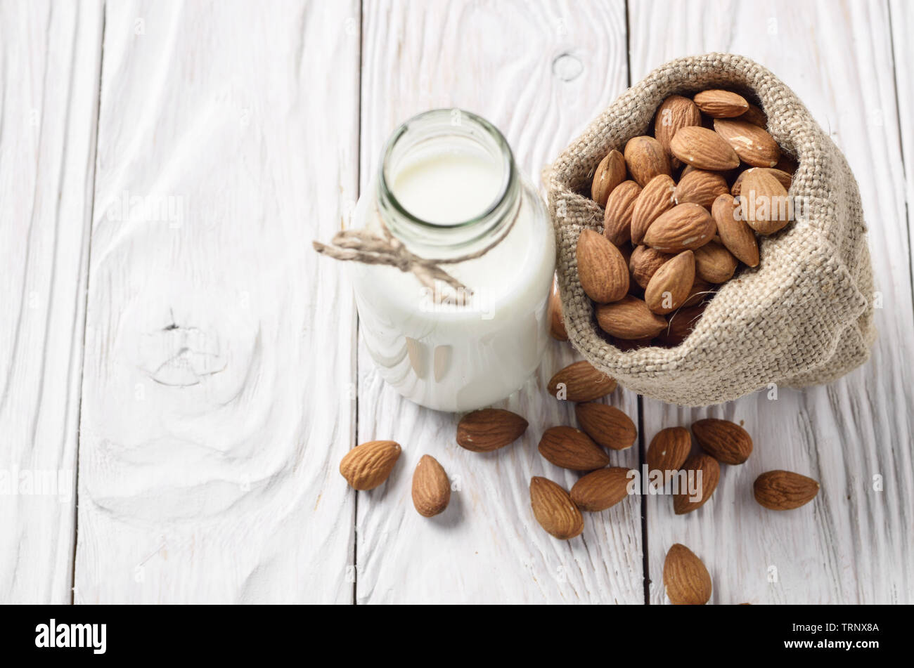 Latte o yogurt in una bottiglia di vetro bianco sul tavolo di legno con le mandorle nel sacco di canapa a parte Foto Stock