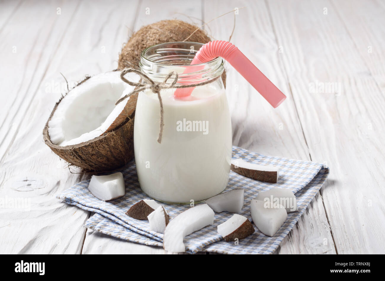 Mason jar di latte o yogurt sul tovagliolo blu su bianco tavolo in legno con noce di cocco a parte Foto Stock