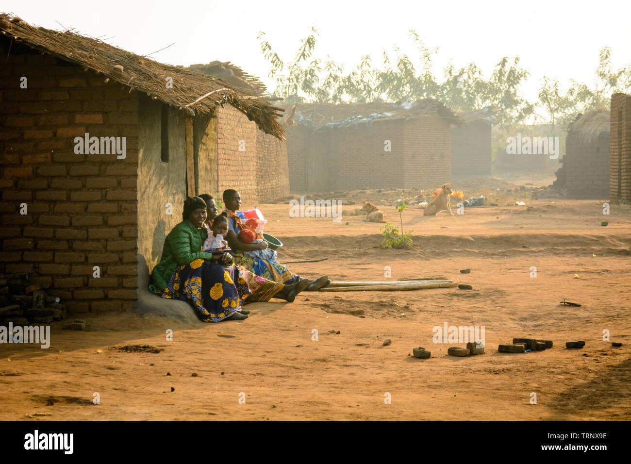 Le donne tenendo i bambini si riuniscono sul passo del loro rifugio in un villaggio del Malawi come il sole tramonta Foto Stock