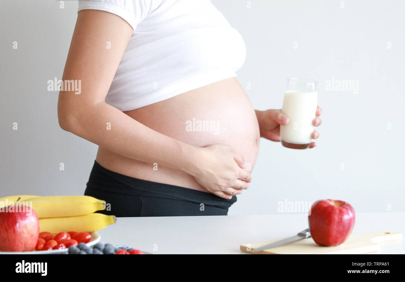 Donna incinta di bere un bicchiere di latte fresco con frutta fresca sul tavolo Foto Stock