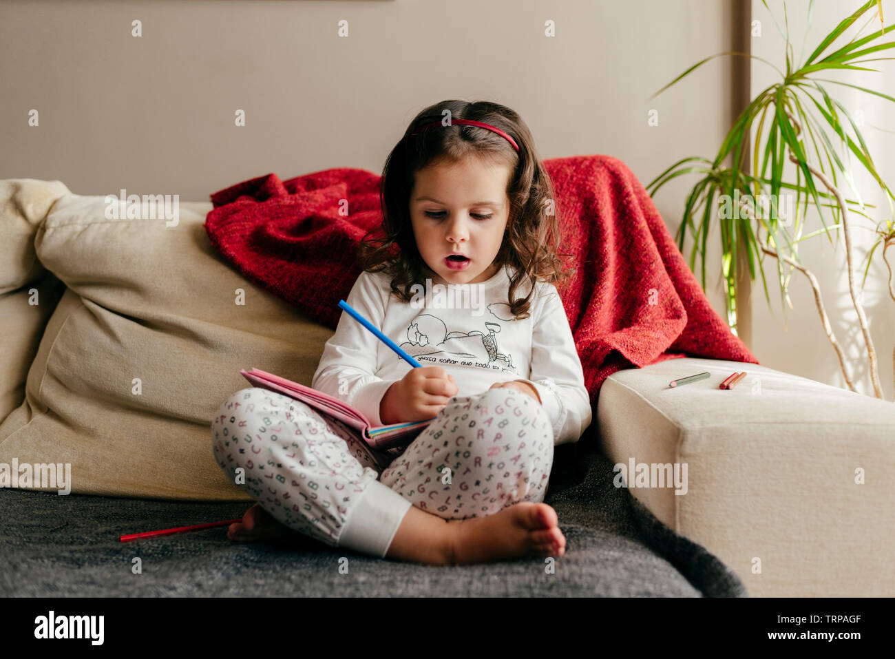 Incantevole piccola ragazza seduta sul lettino e il disegno del notebook Foto Stock