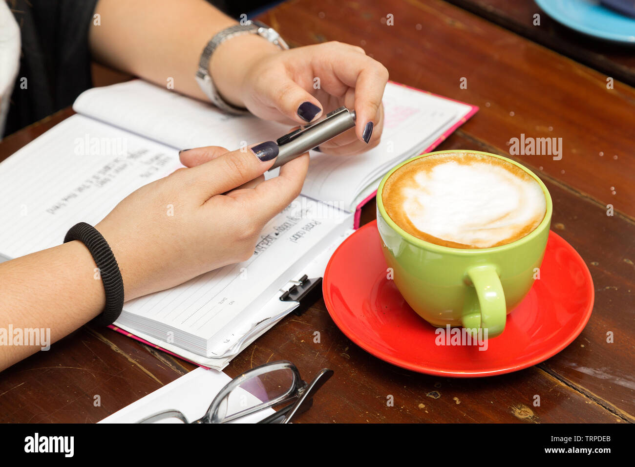 Un incontro informale: tazza di caffè, notebook, mani e una penna sul tavolo, close up Foto Stock