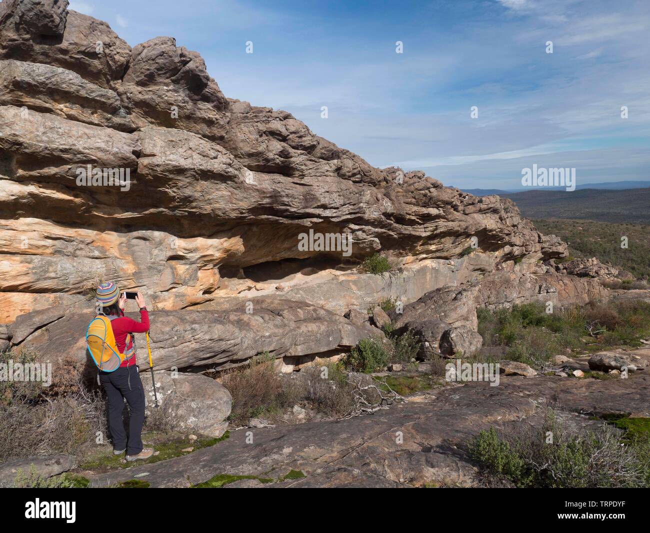 Giovane donna nella parte superiore rossa, pantalone nero e giallo day pack a scattare foto di formazioni rocciose nel Parco Nazionale di Grampians Australia con IPhone. Foto Stock