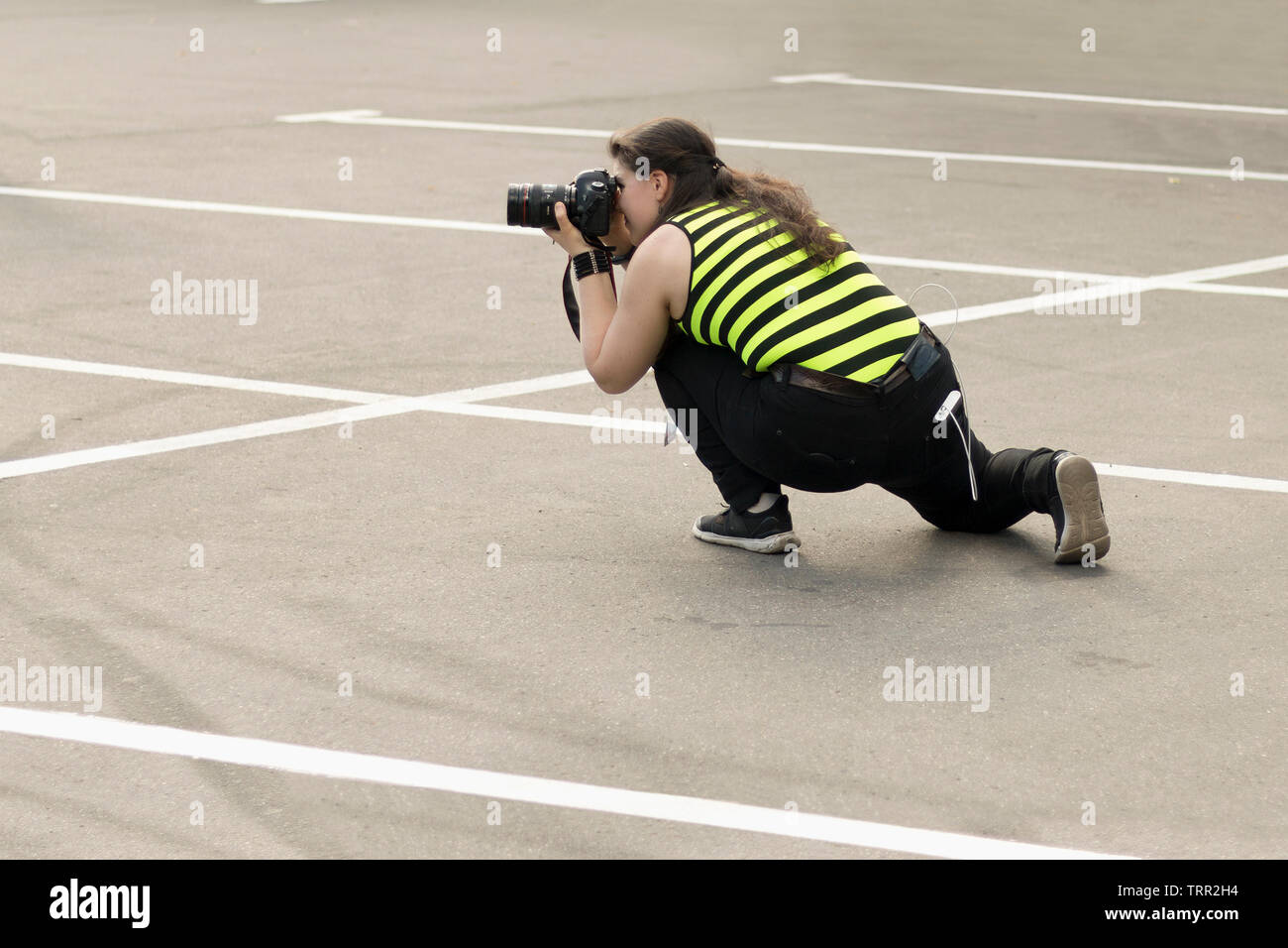 Un fotografo femmina con fotocamera DSLR è segretamente a scattare foto di qualcuno nel parcheggio. Fotografare nascosto, concetto di paparazzi Foto Stock
