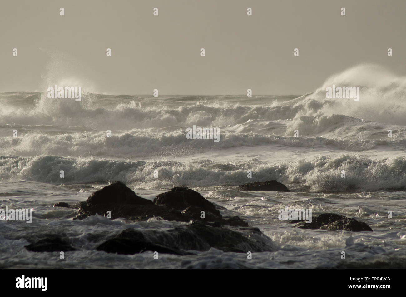 Onde che si infrangono sulla spiaggia con rocce in primo piano Foto Stock