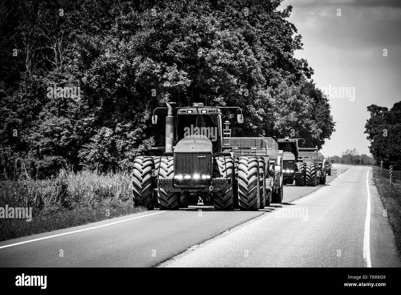 Due enormi trattori agricoli sono carichi di ampia andando giù paese autostrada nel nord-ovest del Mississippi in bianco e nero Foto Stock