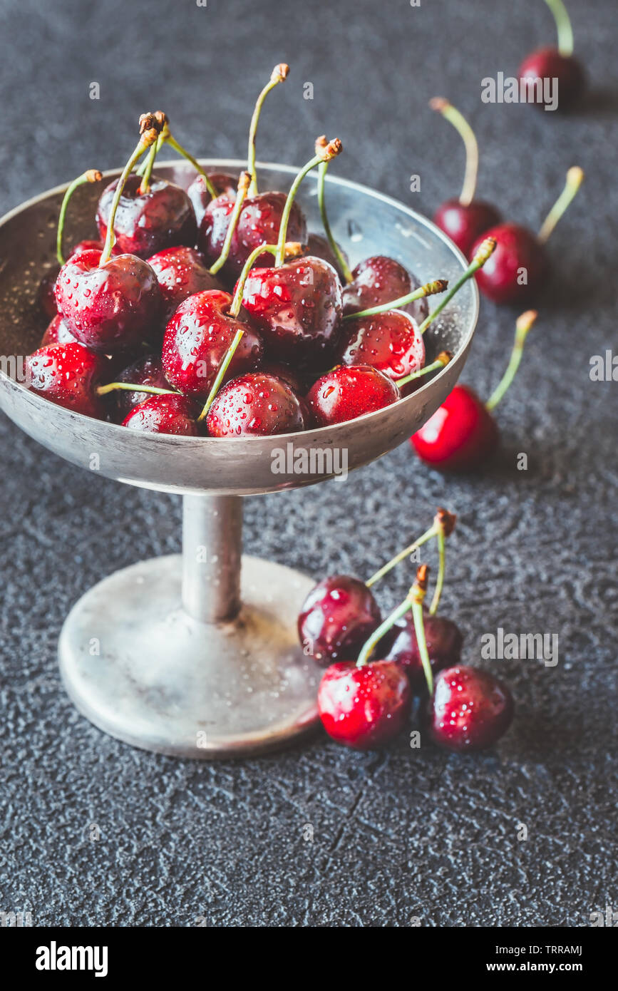 Le ciliege fresche in argento vintage vaso nel buio di sfondo di legno Foto Stock