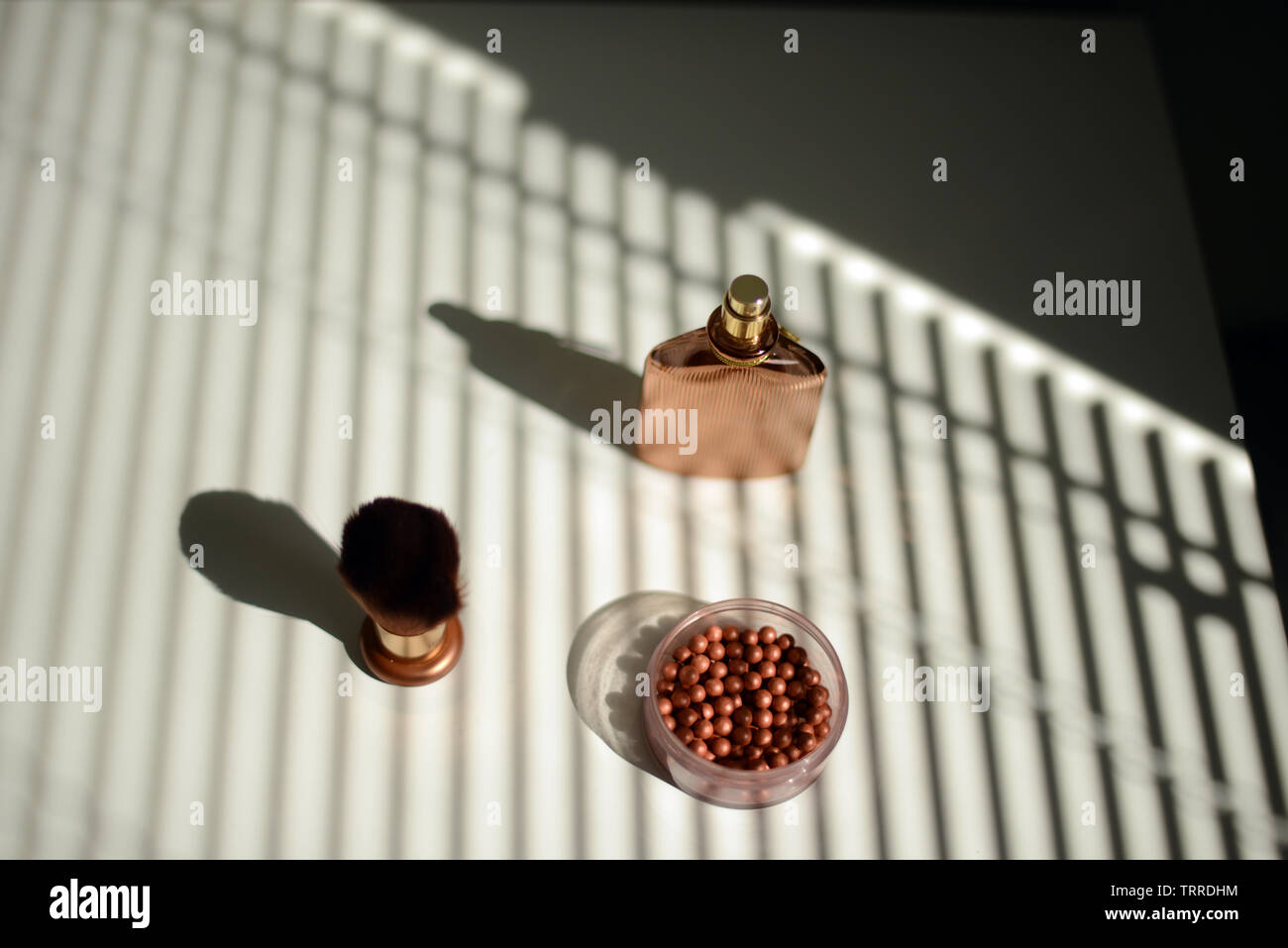 Scatola di perle di imbrunimento, make-up pennello e una bottiglia di profumo su un tavolo bianco in presenza di luce solare proveniente attraverso persiane Foto Stock